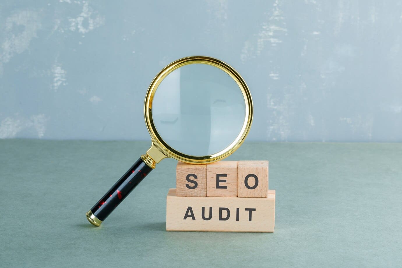 SEO vs PPC analysis concept with magnifying glass highlighting wooden blocks labeled "SEO Audit," representing online marketing strategies and evaluation.